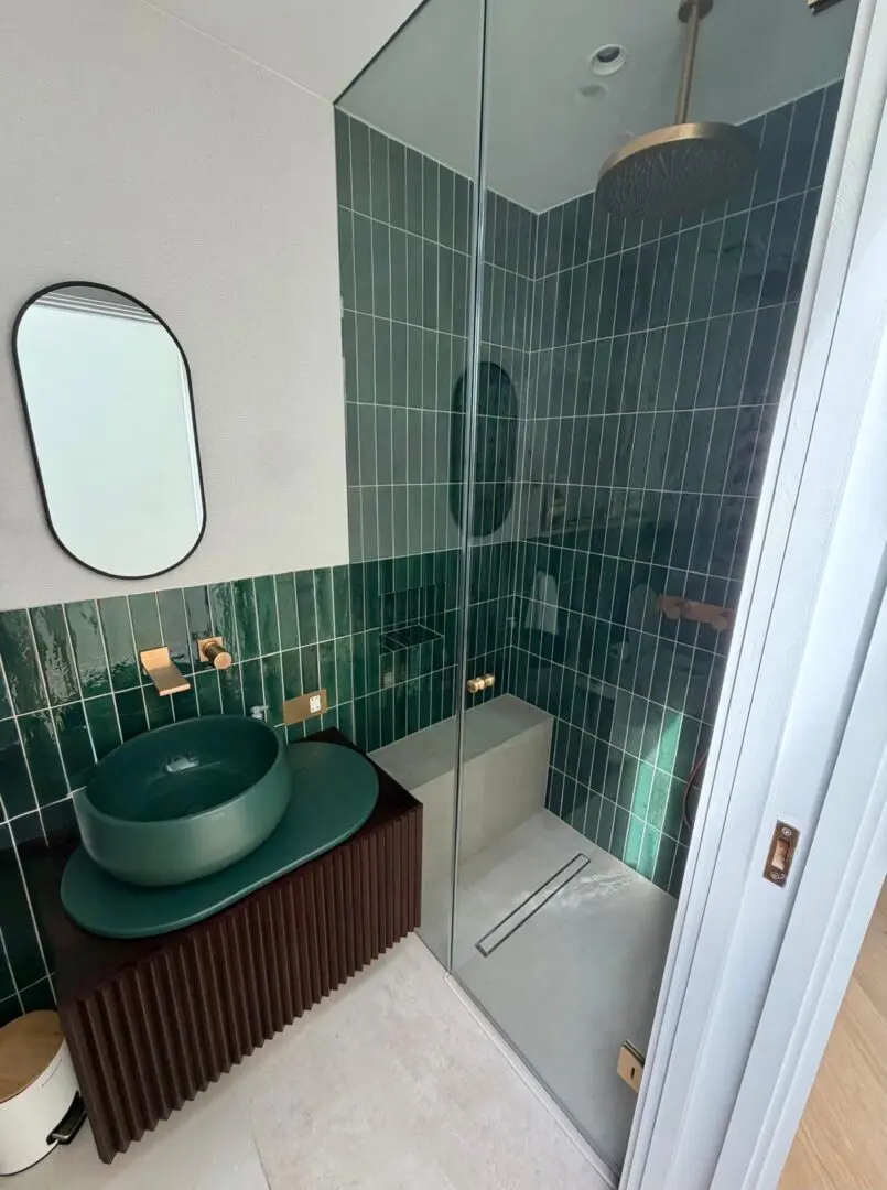 Bathroom with a green sink sitting under a mirror next to a walk-in shower, with taps