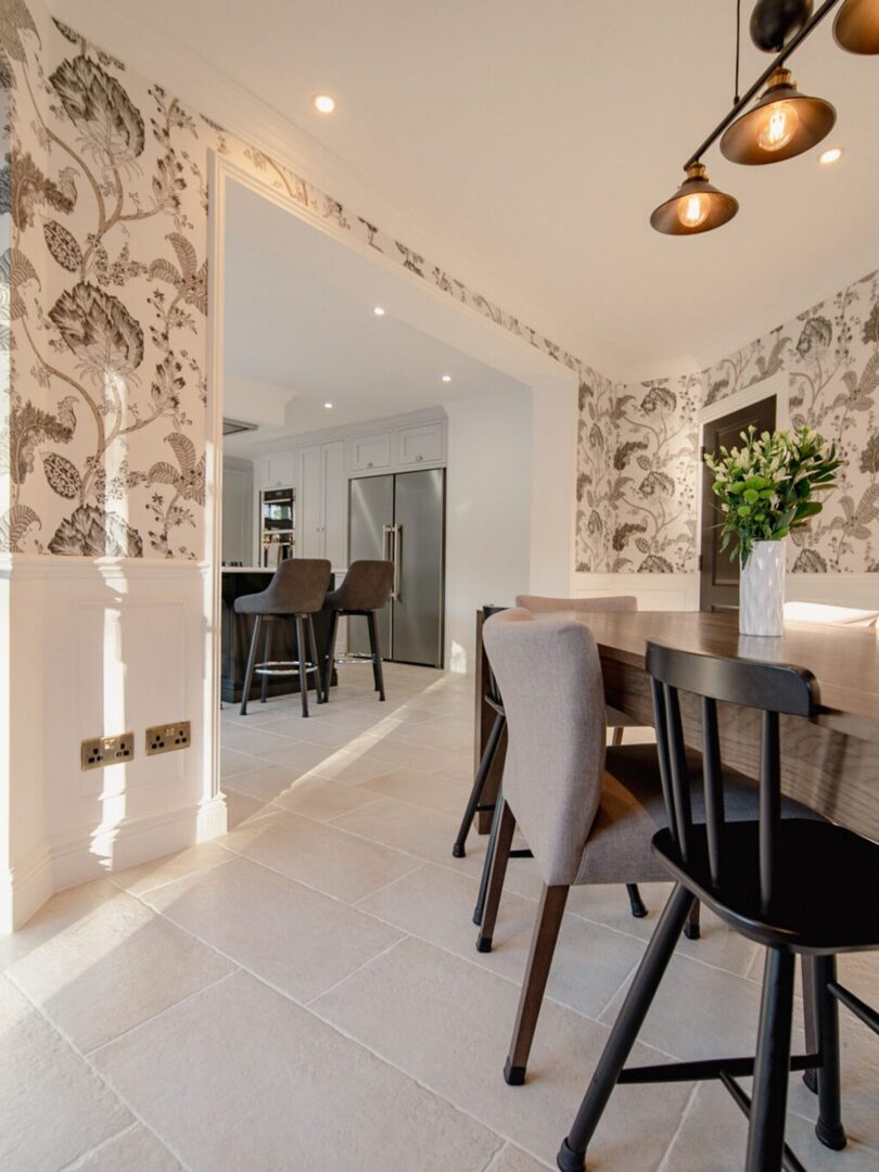 Dining room with a wooden table and chairs, a flower vase on the table, a wall with a design