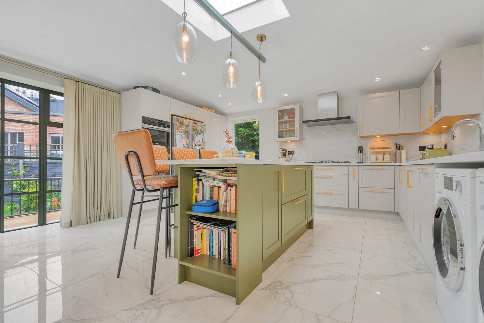 Kitchen with a table and chairs in it, a bookshelf with books, a washing machine, a sink with a tap
