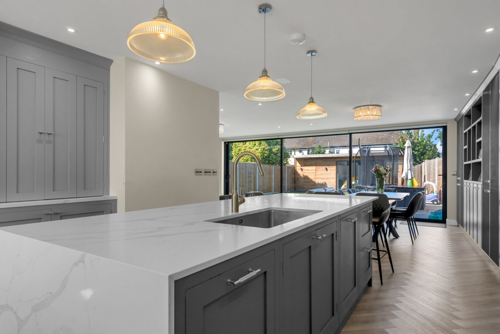 Kitchen with a large island in the middle of it, featuring a sink and tap, cupboards, a dining table
