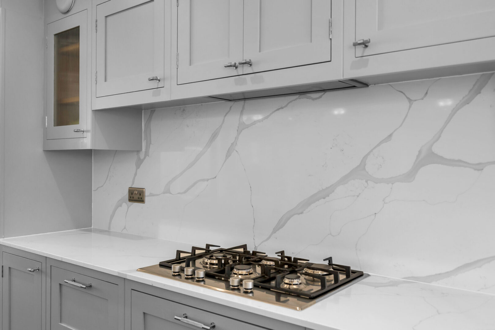 Kitchen with white cabinets and a stove top oven, with a marble backsplash featuring a unique design