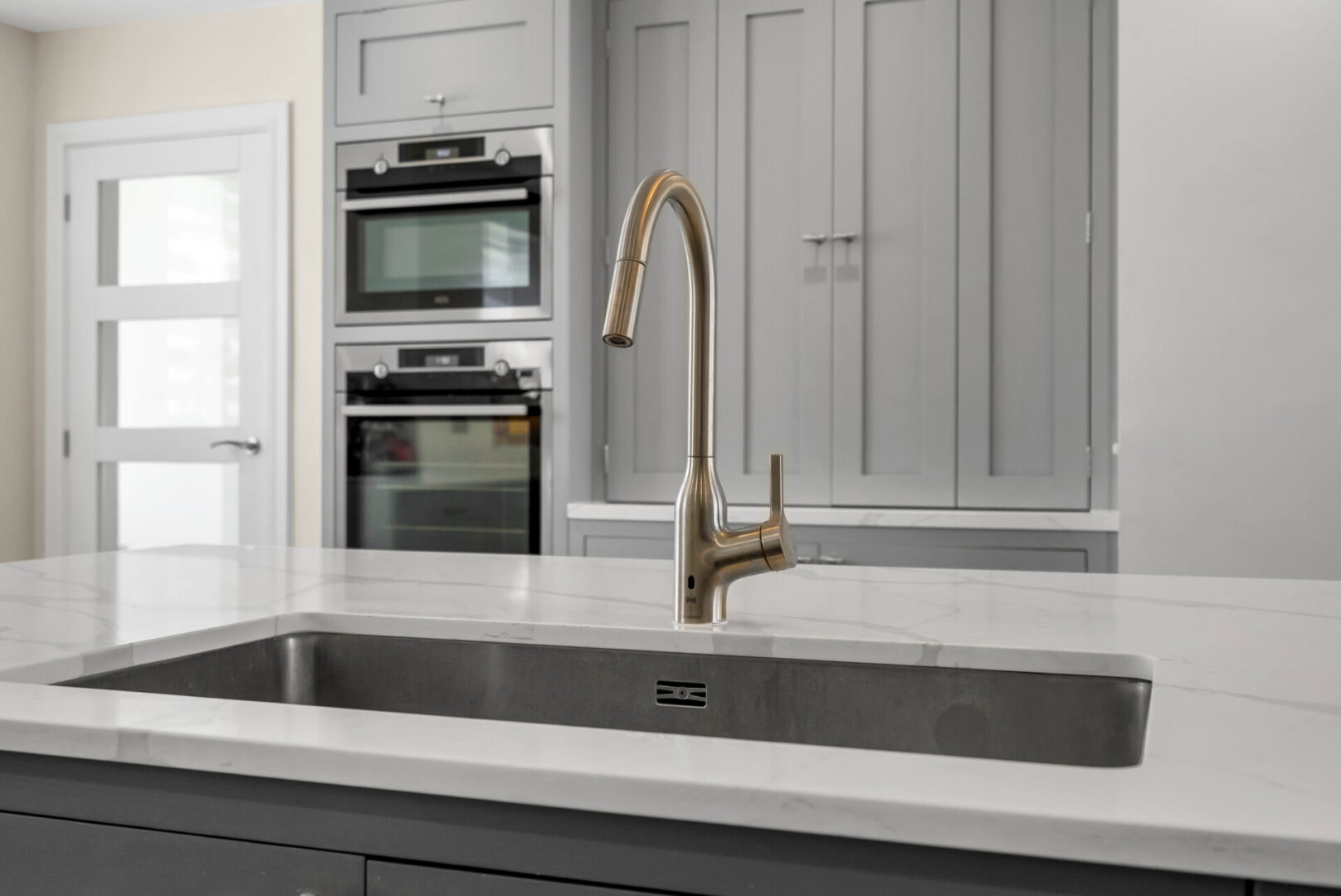 Kitchen with a stainless steel sink and a faucet, a countertop, cupboards, a door, and a wall