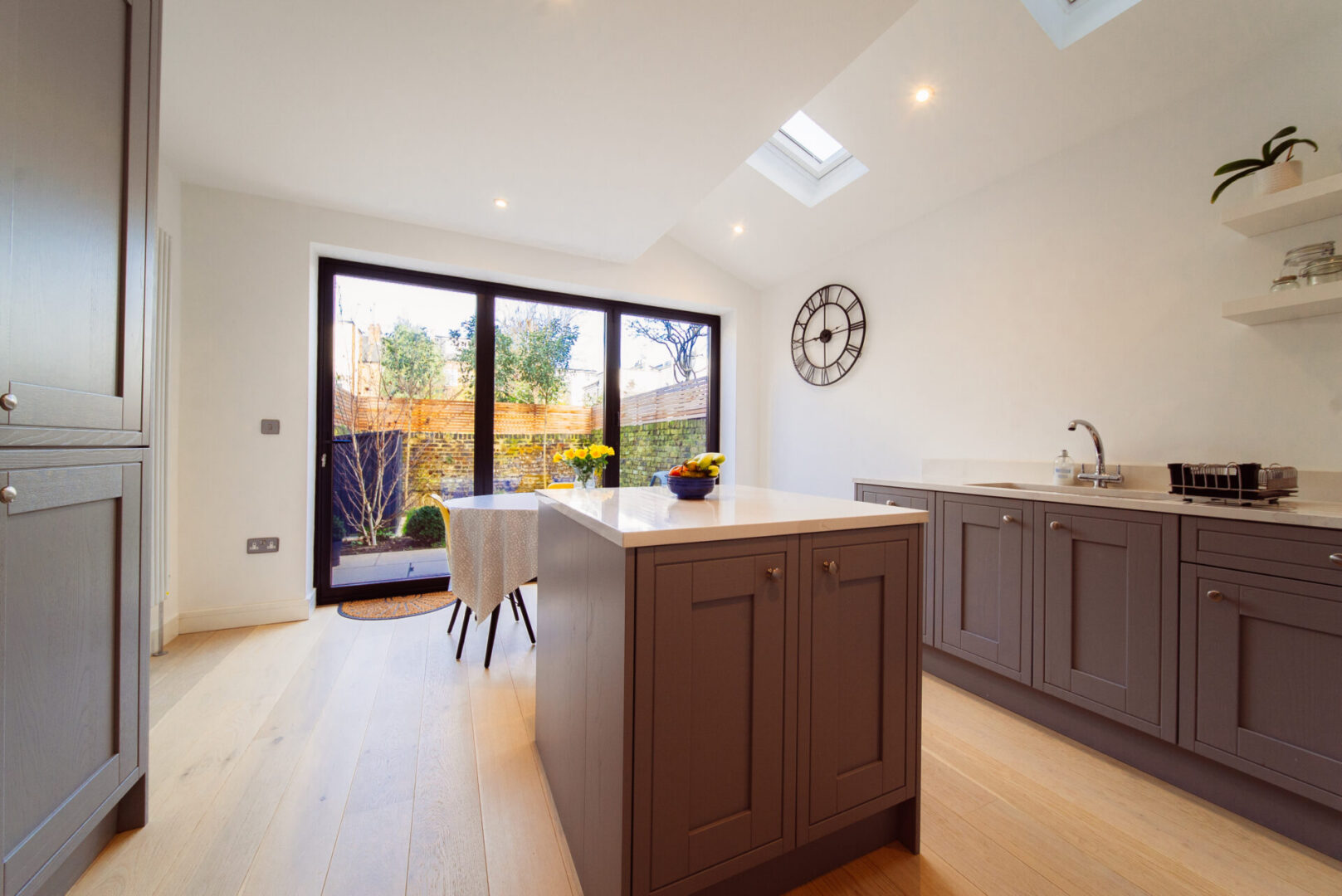Kitchen with a large island in the middle of it, featuring a sink, tap, flower vase, fruits in a bowl