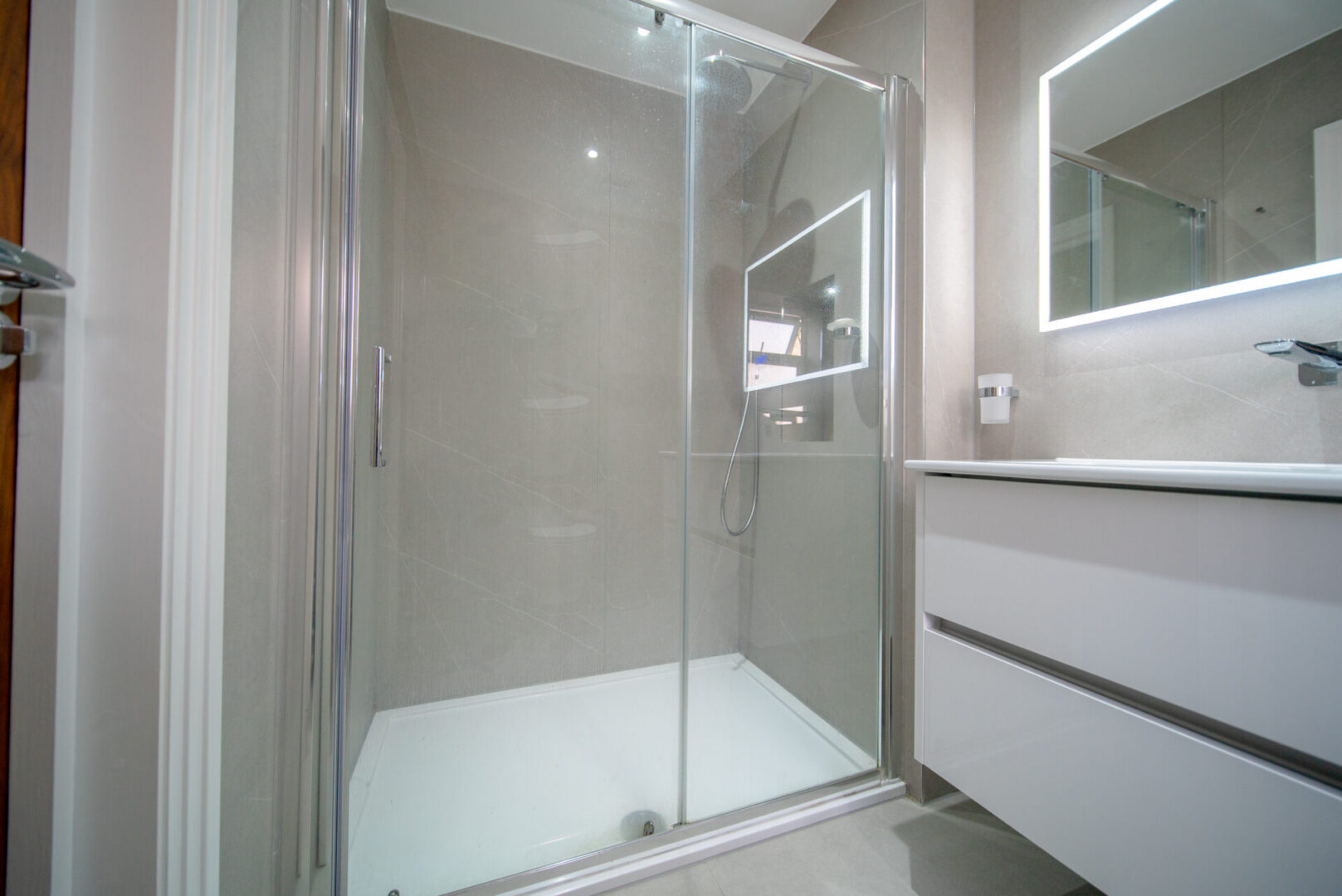 Bathroom with a walk-in shower next to a sink, a mirror on the wall, a tap, a glass door