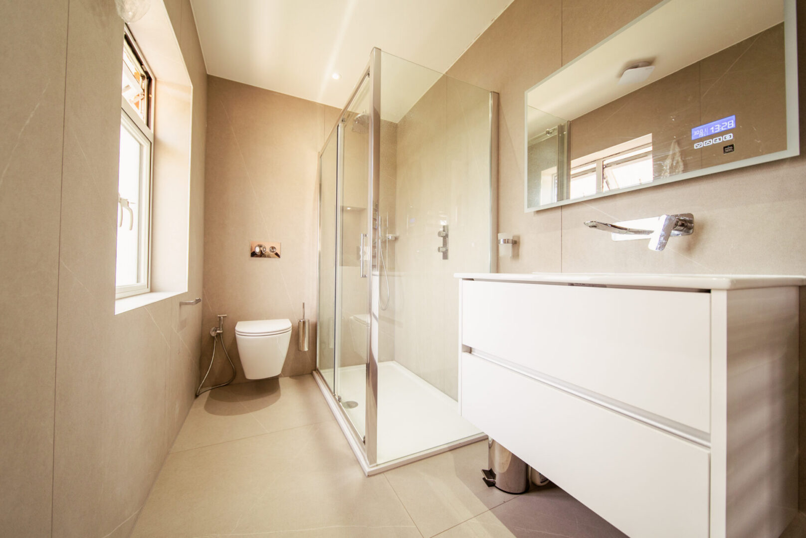 Bathroom with a toilet, sink, shower, glass door, window, dustbin, tap, mirror and electric lights to the roof