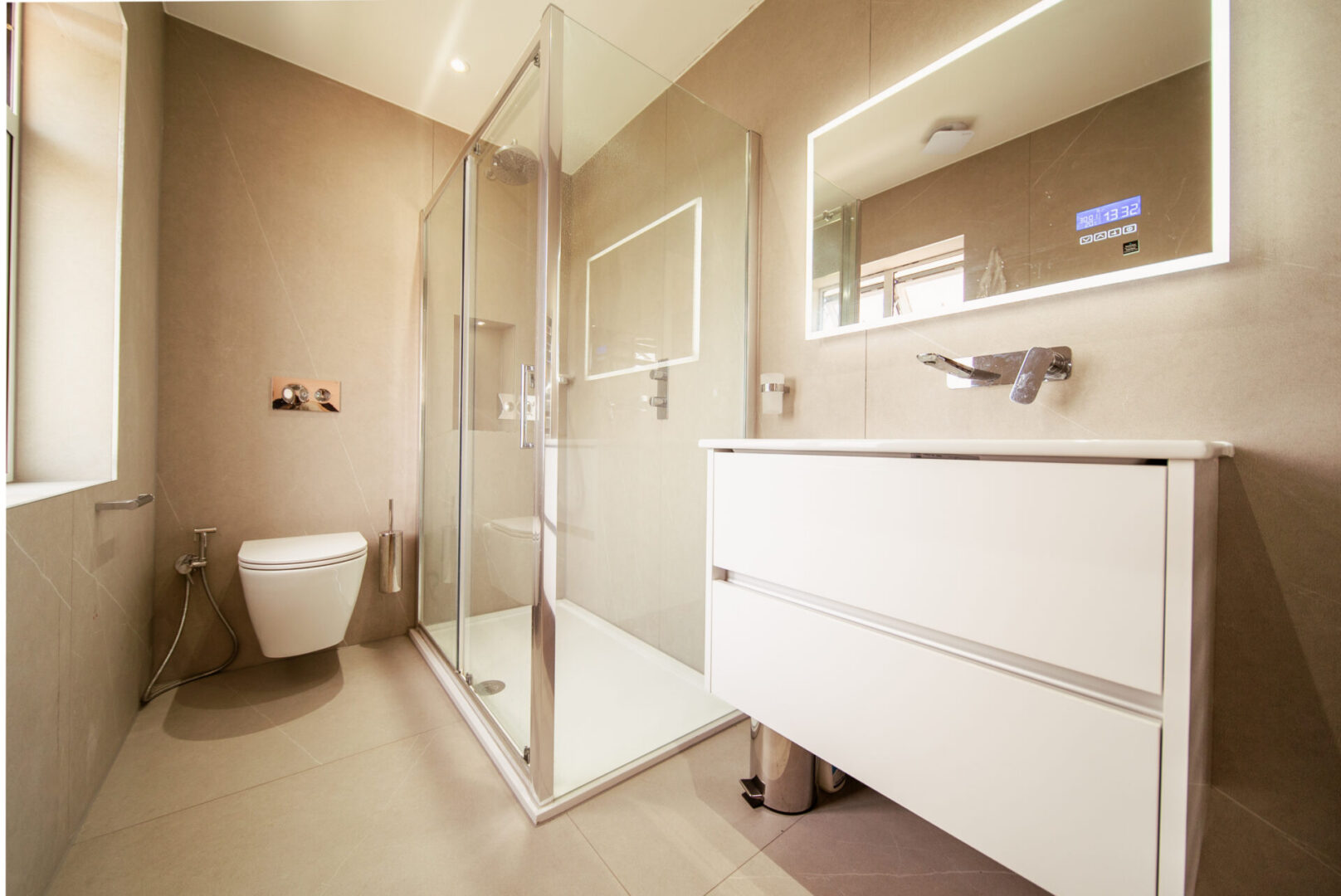 Bathroom with a toilet, sink, shower, glass door, taps, mirror, window, dustbin and electric lights to the roof